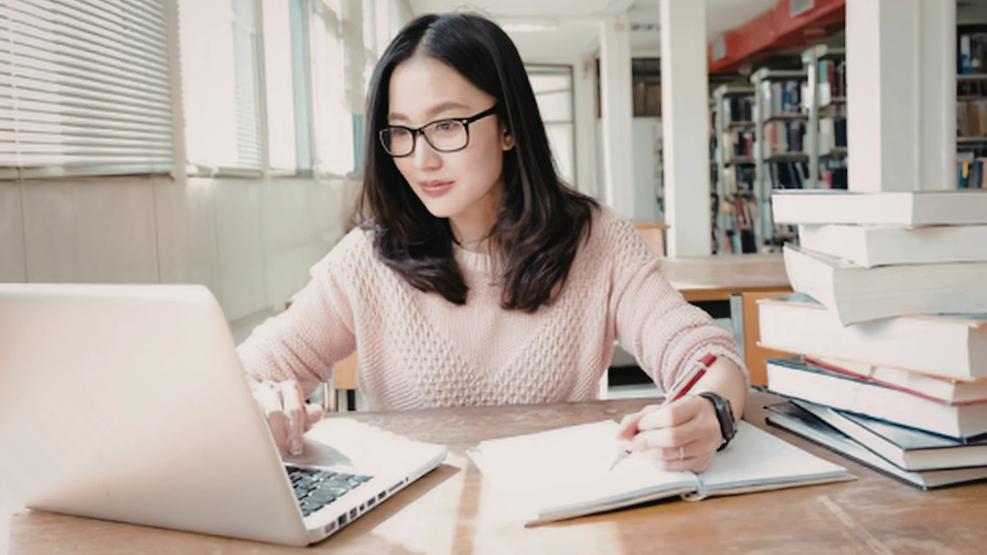 Frau arbeitet konzentriert mit Laptop und Notizbuch an einem wissenschaftlichen Text.